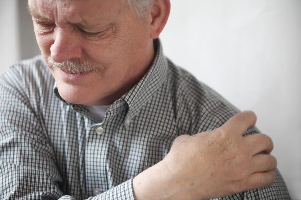 older man holding shoulder and wincing in pain