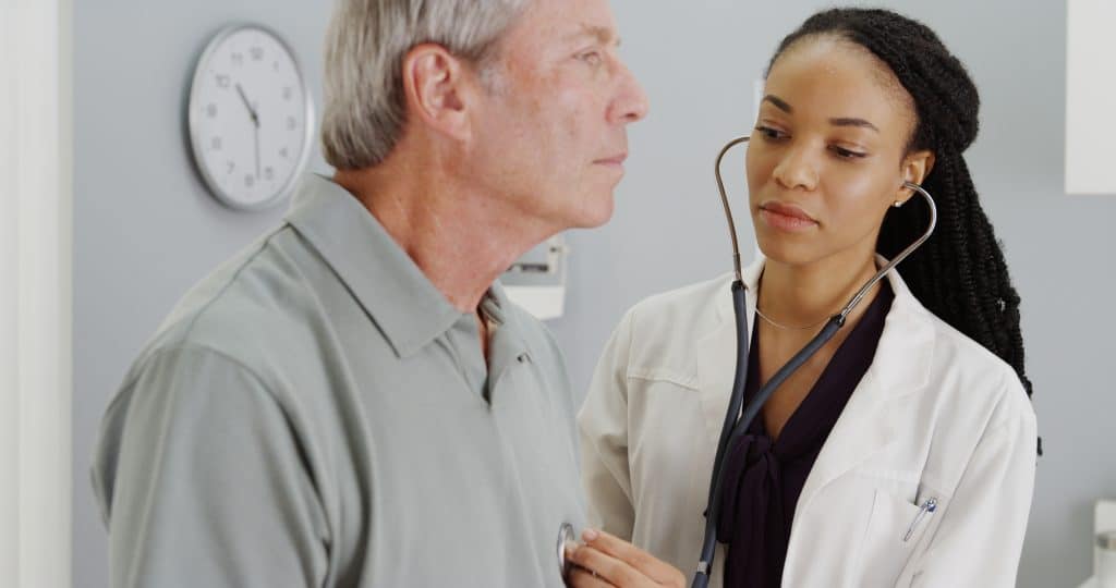 black doctor listening to senior man's chest with stethoscope