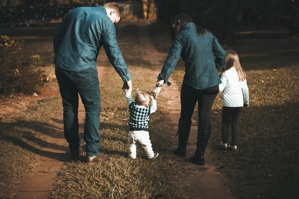 A young family of four walks along the grass up to their home in the distance.