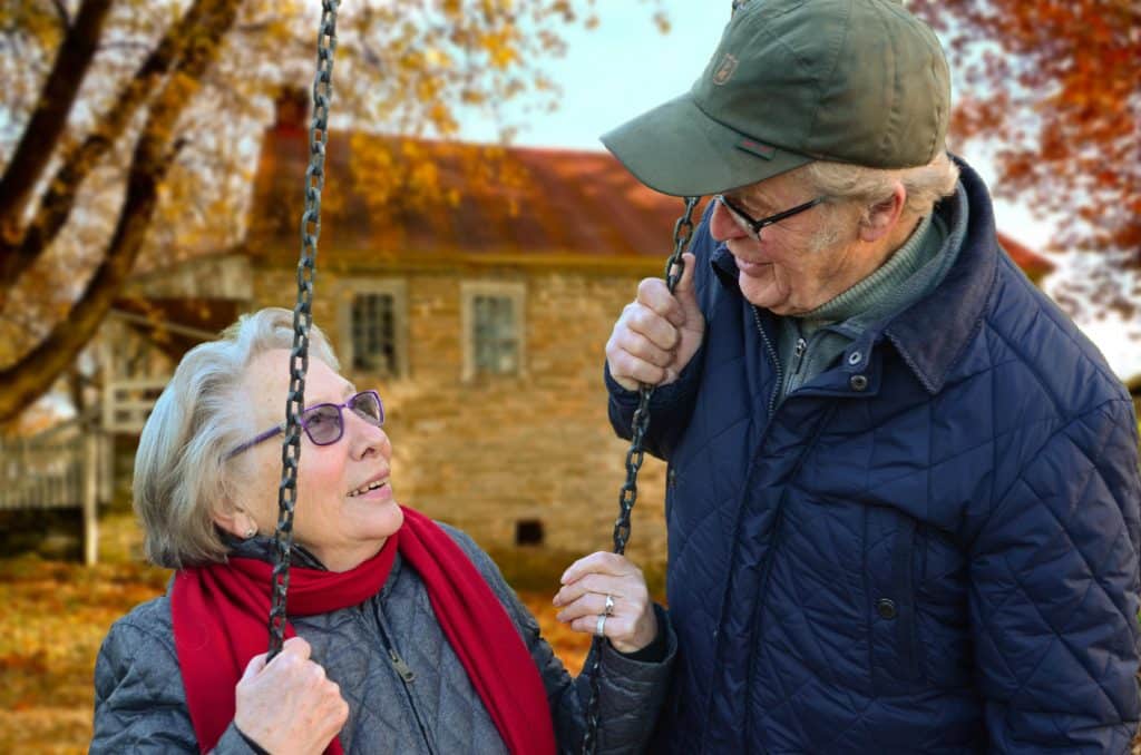 An elderly couple on a swing outside.